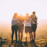Family Bonding - four person hands wrap around shoulders while looking at sunset