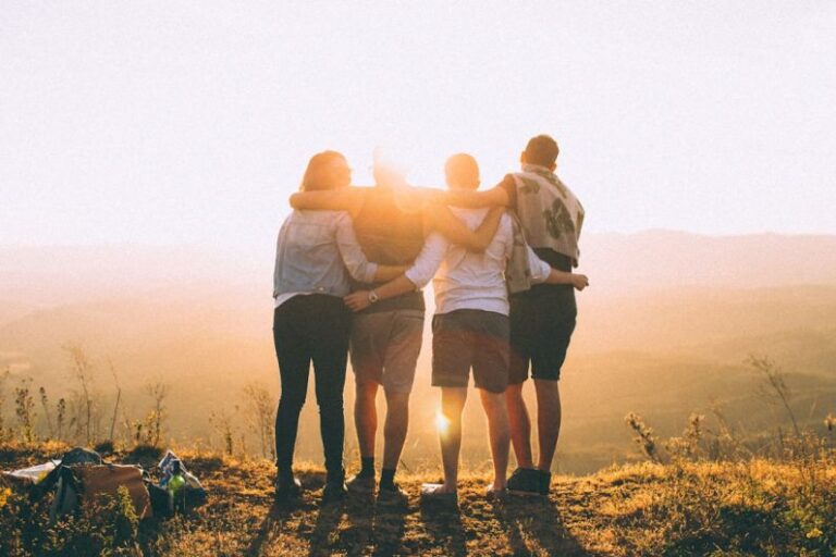 Family Bonding - four person hands wrap around shoulders while looking at sunset