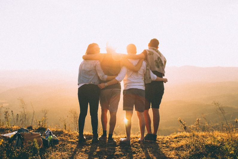 Family Bonding - four person hands wrap around shoulders while looking at sunset