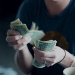 Income - focus photography of person counting dollar banknotes