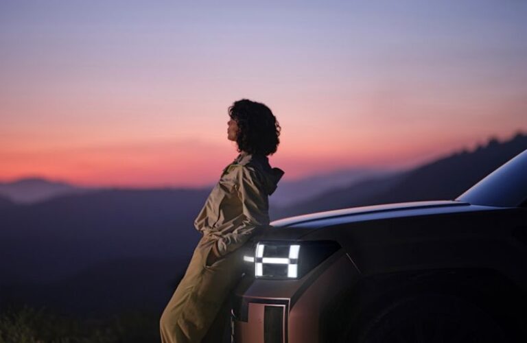 Electric Vehicles - a woman sitting on the hood of a car