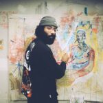 Artists - man in black and white sweater standing beside wall with graffiti