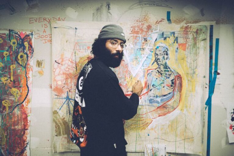 Artists - man in black and white sweater standing beside wall with graffiti