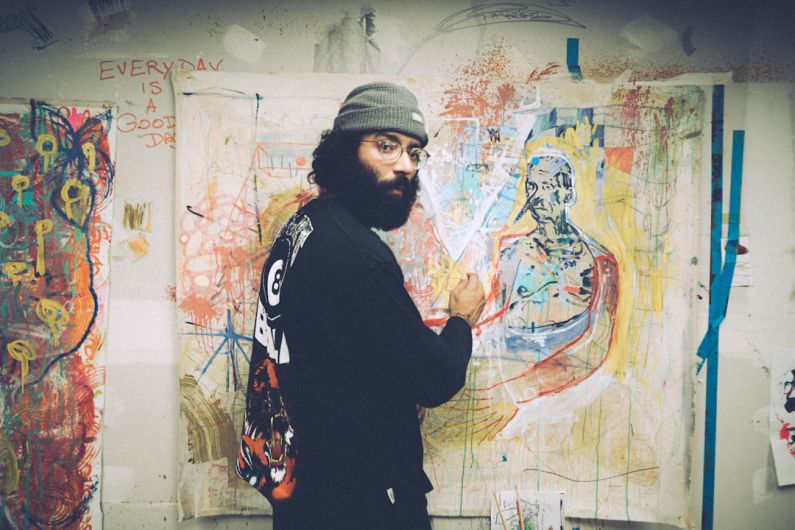 Artists - man in black and white sweater standing beside wall with graffiti