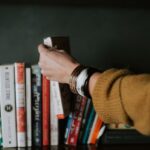 Reading - person picking white and red book on bookshelf