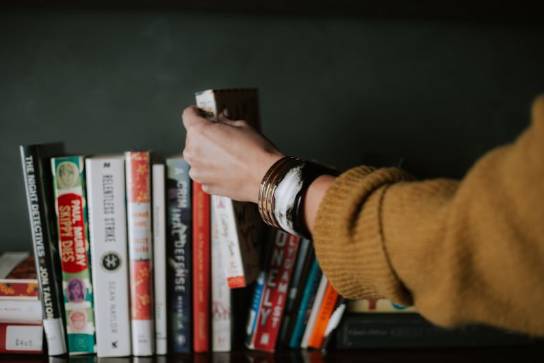 Reading - person picking white and red book on bookshelf
