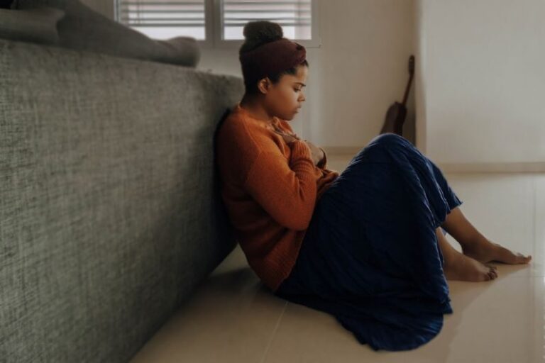 Anxiety - man in orange long sleeve shirt sitting on gray couch