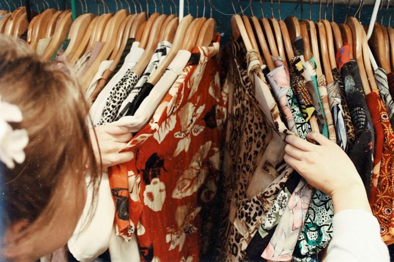 Thrift Shopping - person holding assorted clothes in wooden hanger